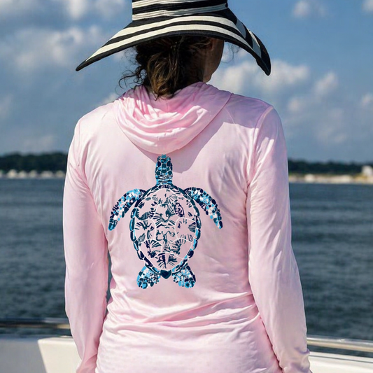 Model wearing a pink hoodie with a blue turtle on the back while standing on a boat