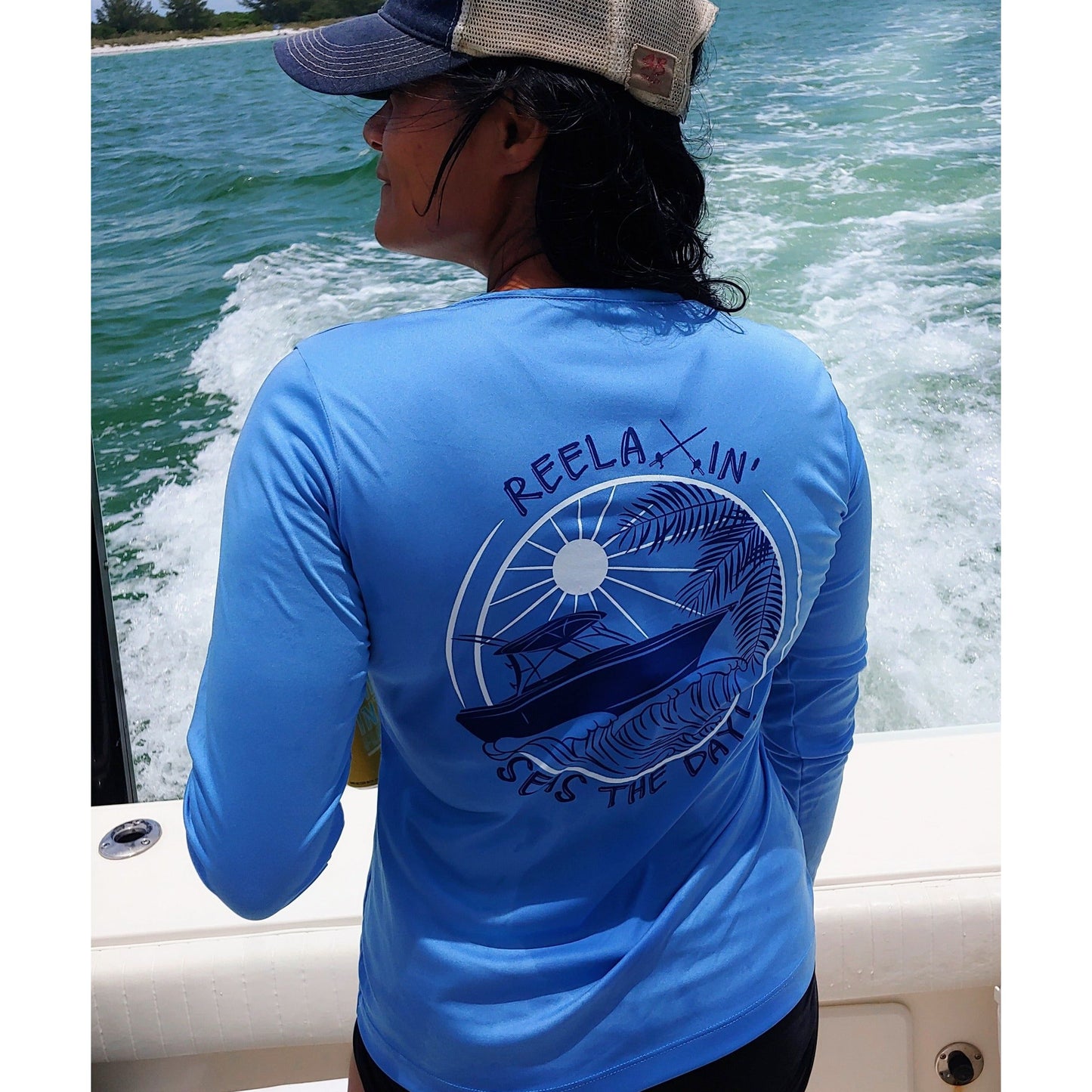 Model wearing ladies light blue long sleeve V-neck performance dry-fit shirt with Reelaxin’ – Seas the Day logo on the back.
