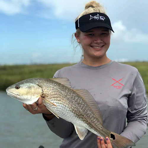 Lady Angler catching a Redfish and wearing a Ladies Performance  50+UV Fishing Shirt and a Tarpon Performance Visor