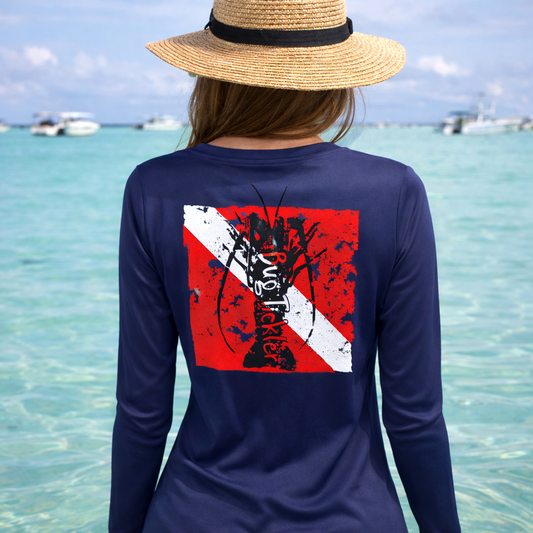 Woman wearing a V-neck navy long sleeve performance lobster shirt and a red-and-white diver down flag “Bug Tickler” graphic on the back, facing the water.