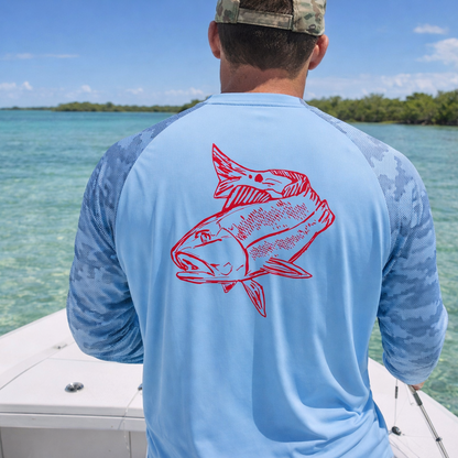 Fisherman wearing a Redfish light blue performance long sleeve shirt with camo sleeves, standing on a boat in the keys