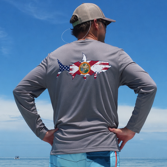 Model wearing a gray long-sleeve UPF 50 sun shirt with a tarpon fish and State of Florida graphic design on the back, standing on a boat in Key West.