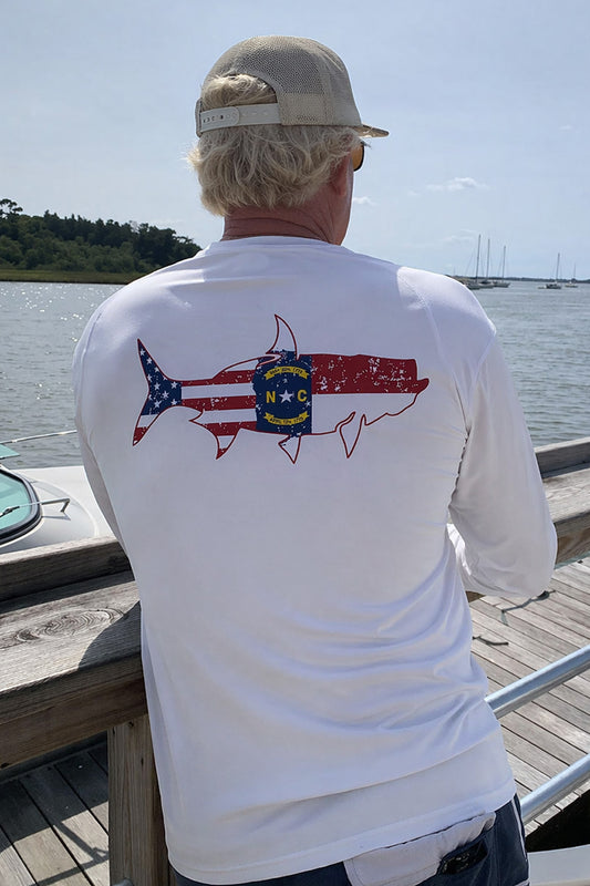 Man wearing a white long-sleeve UPF 50 performance sun shirt with a tarpon fish and State of North Carolina Flag graphic design on the back.