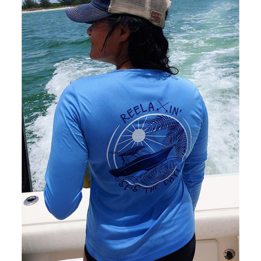Model wearing ladies light blue long sleeve V-neck performance dry-fit shirt with Reelaxin’ – Seas the Day logo on the back.