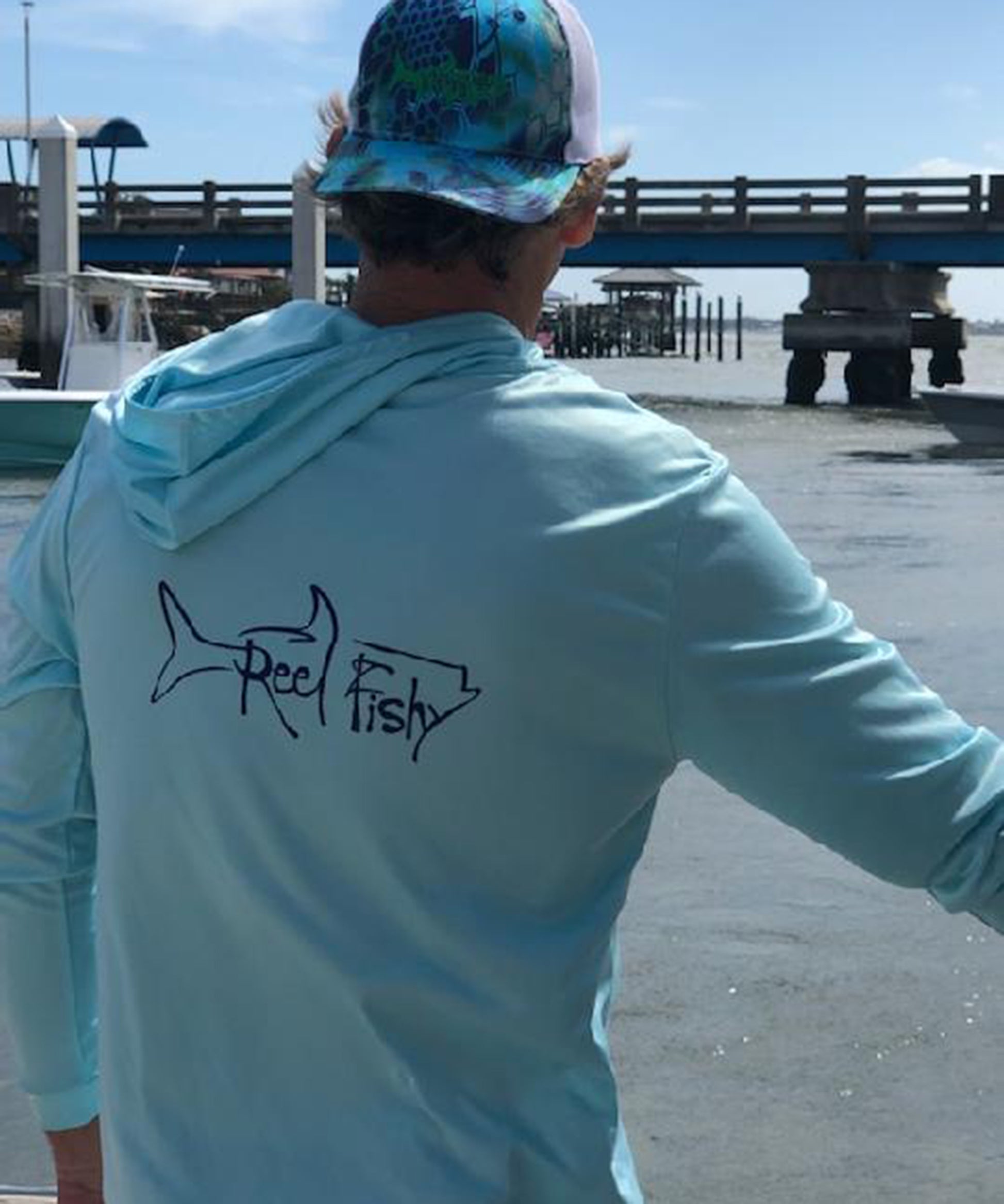Model wearing light blue Reel Fishy Tarpon performance fishing hoodie with long sleeves and 50+ UPF sun protection